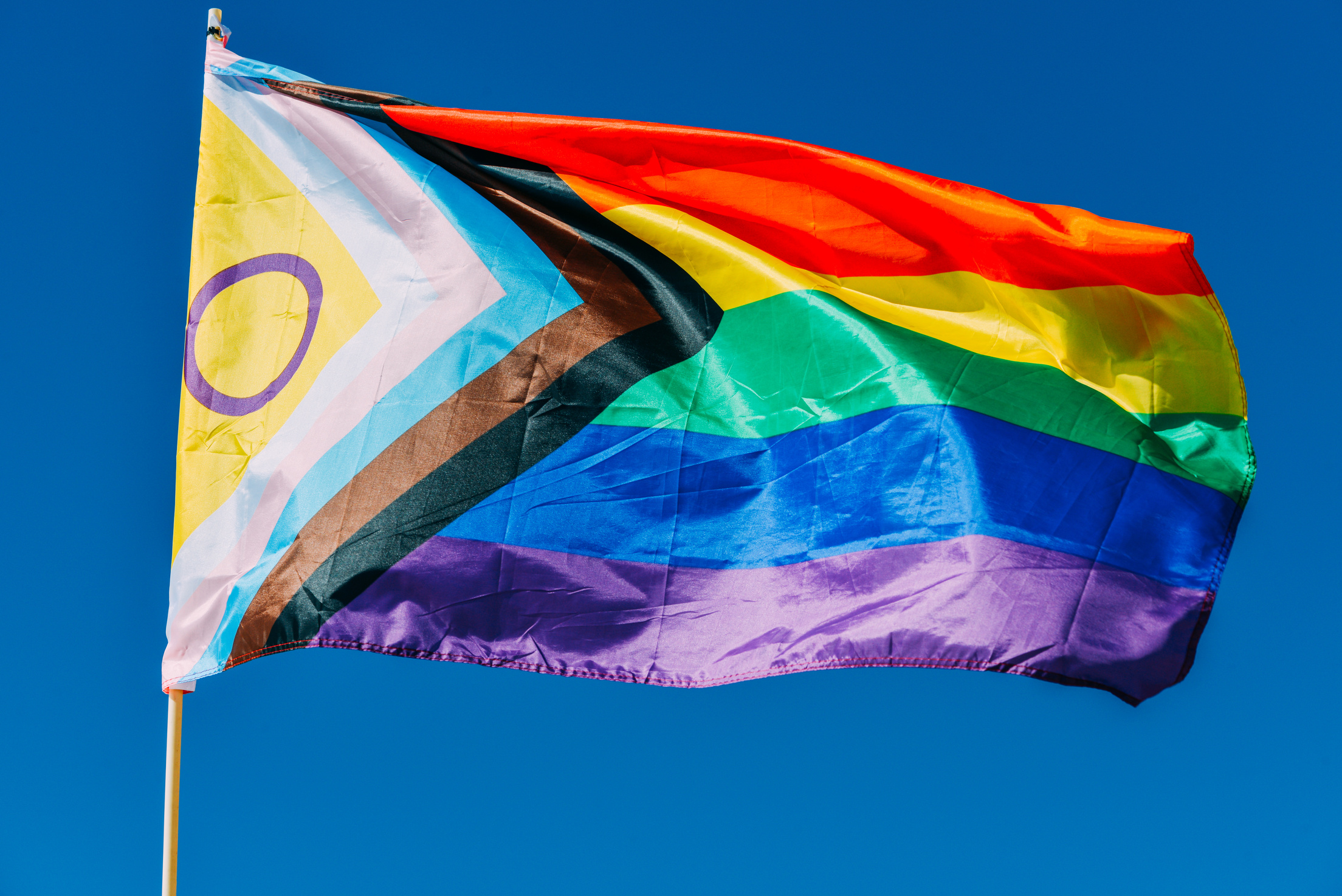 Progress LGBTQ progress rainbow flag waving in the wind against blue sky